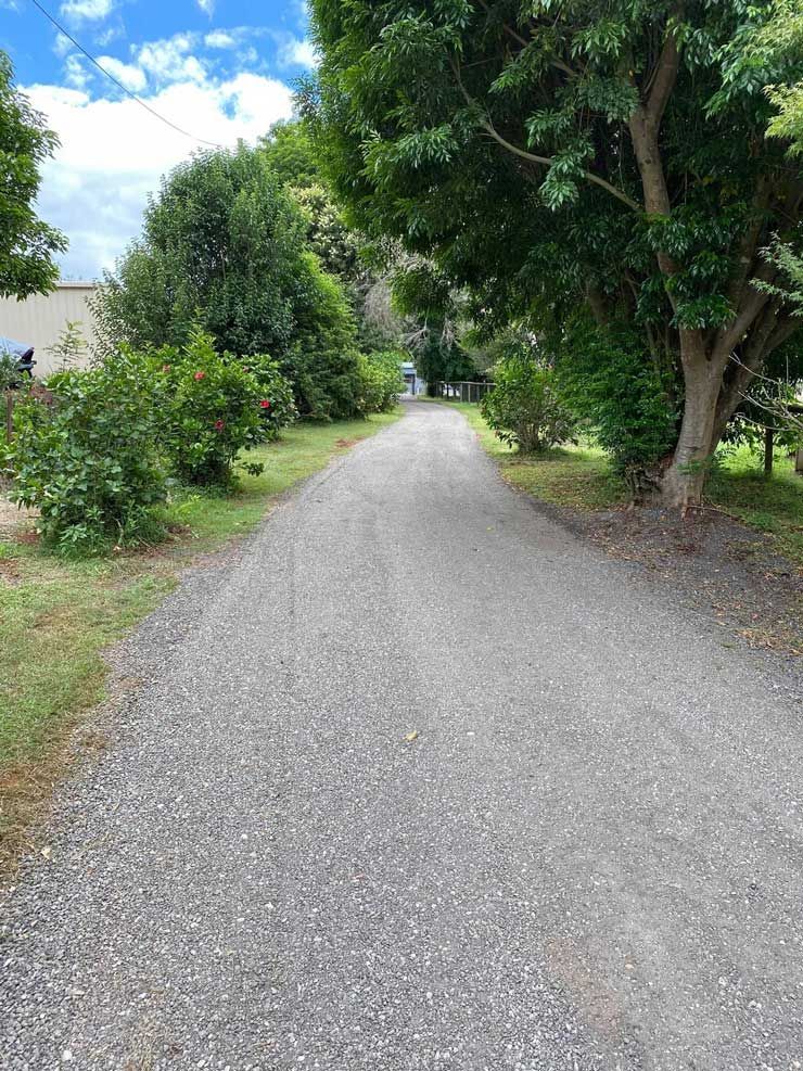 A Gravel Road Surrounded by Trees and Grass on a Sunny Day — Caloundra Landscape Supplies in Caloundra, QLD