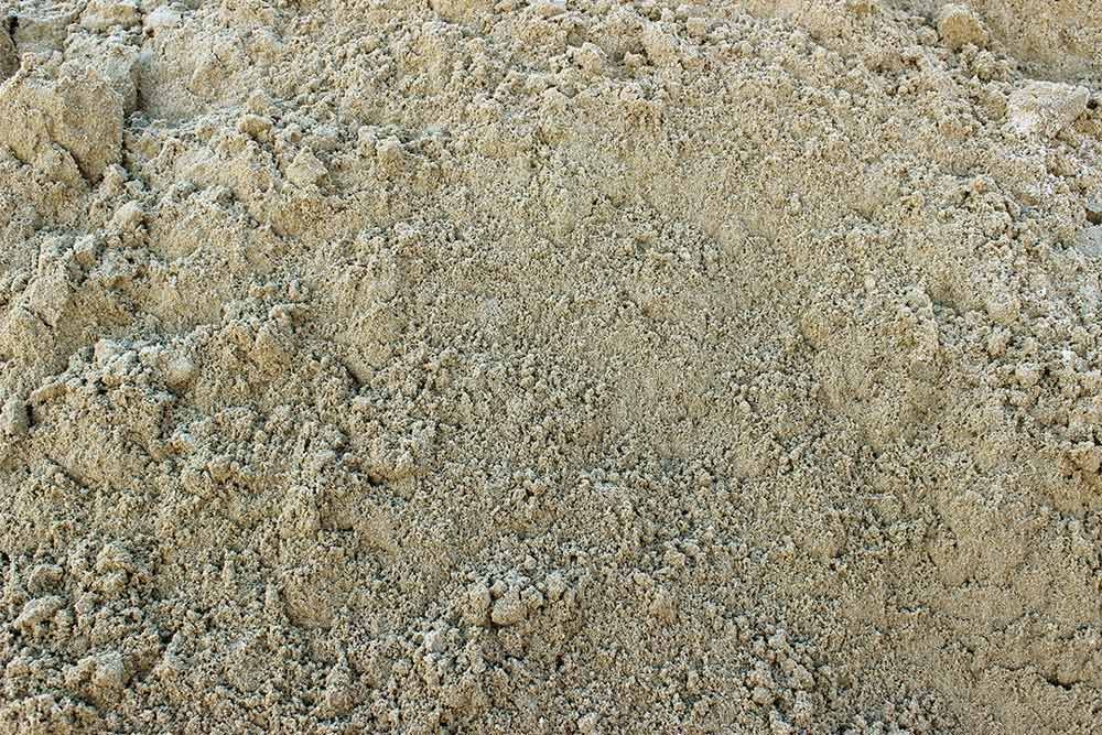 Close-up of a pile of beige sand, showing a rough, granular texture.