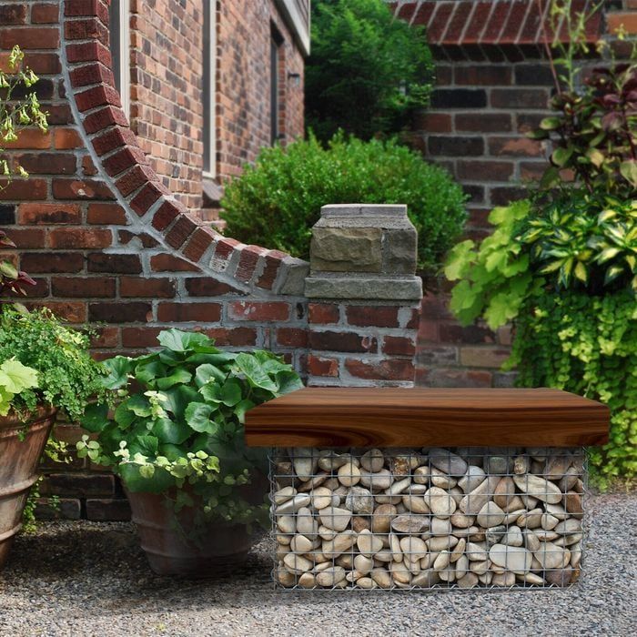 Bench made of stones and wood in an outdoor garden setting with brick wall.