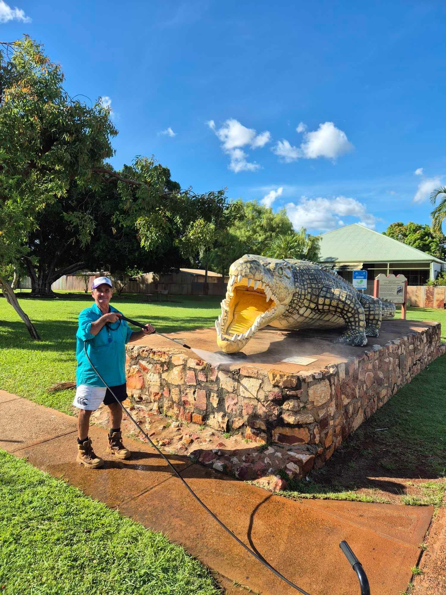 A Man is Standing in Front of a Statue of a Crocodile With Its Mouth Open — NQW Services In Cardwell, QLD