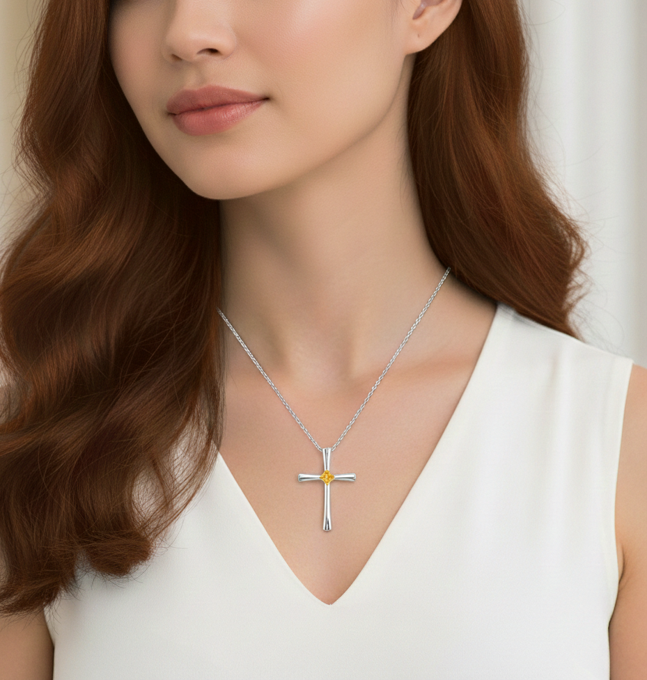 一位身穿白色上衣的人戴著一條銀色十字架吊墜項鍊,項鍊中央鑲嵌著一顆小小的黃色寶石。