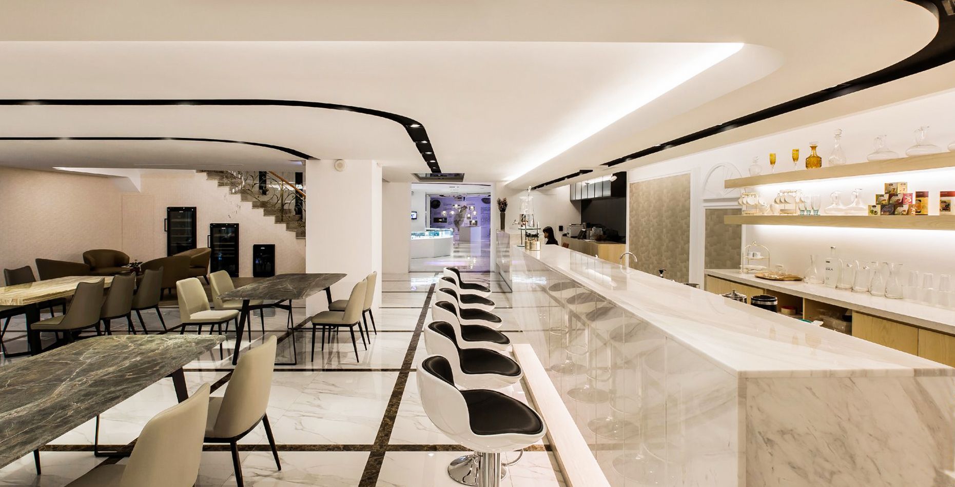 一個長長的現代酒吧，配有大理石檯面、吧台座椅和餐桌，並以黑色燈光和樓梯作為點綴。
