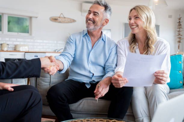 A man and woman are shaking hands with a real estate agent while sitting on a couch.