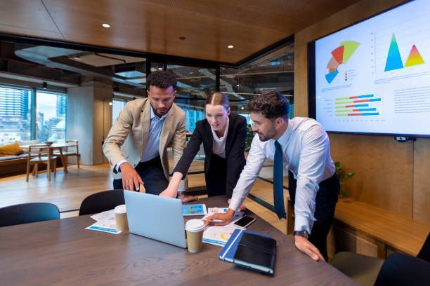 A group of people are standing around a table looking at a laptop computer.
