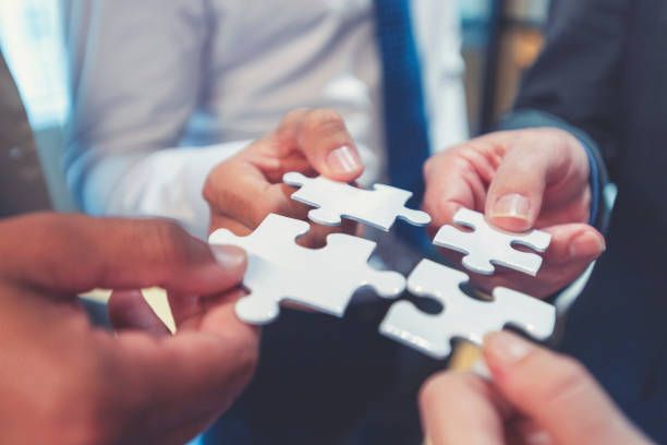 A group of people are holding white puzzle pieces in their hands.