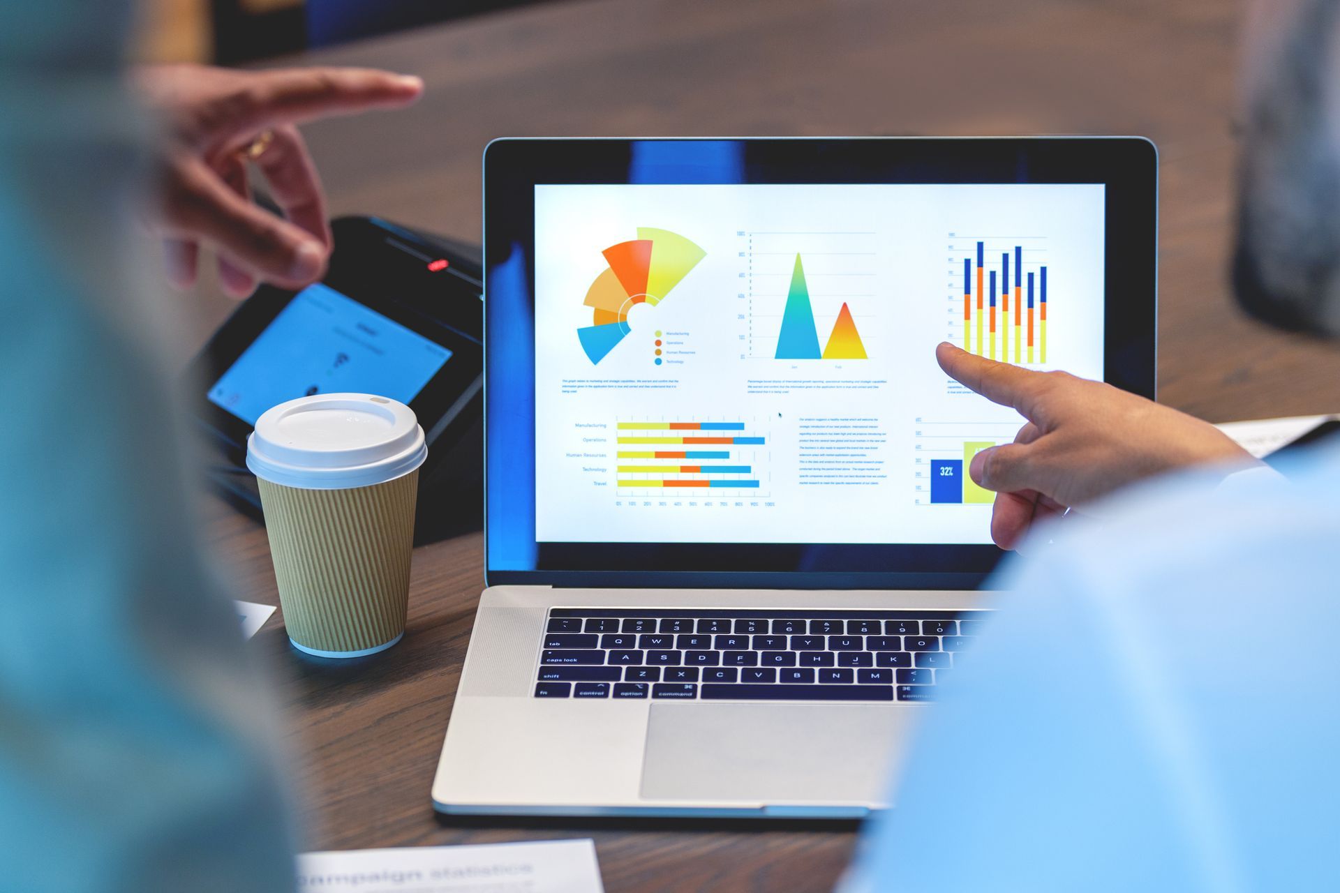 A person is pointing at a laptop computer with graphs on the screen.