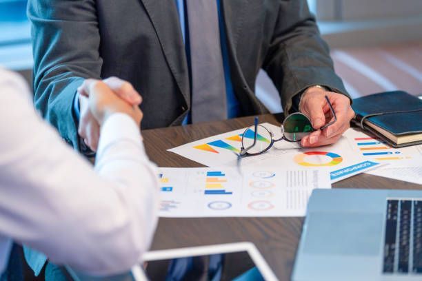 A man in a suit and tie is shaking hands with another man while sitting at a table.