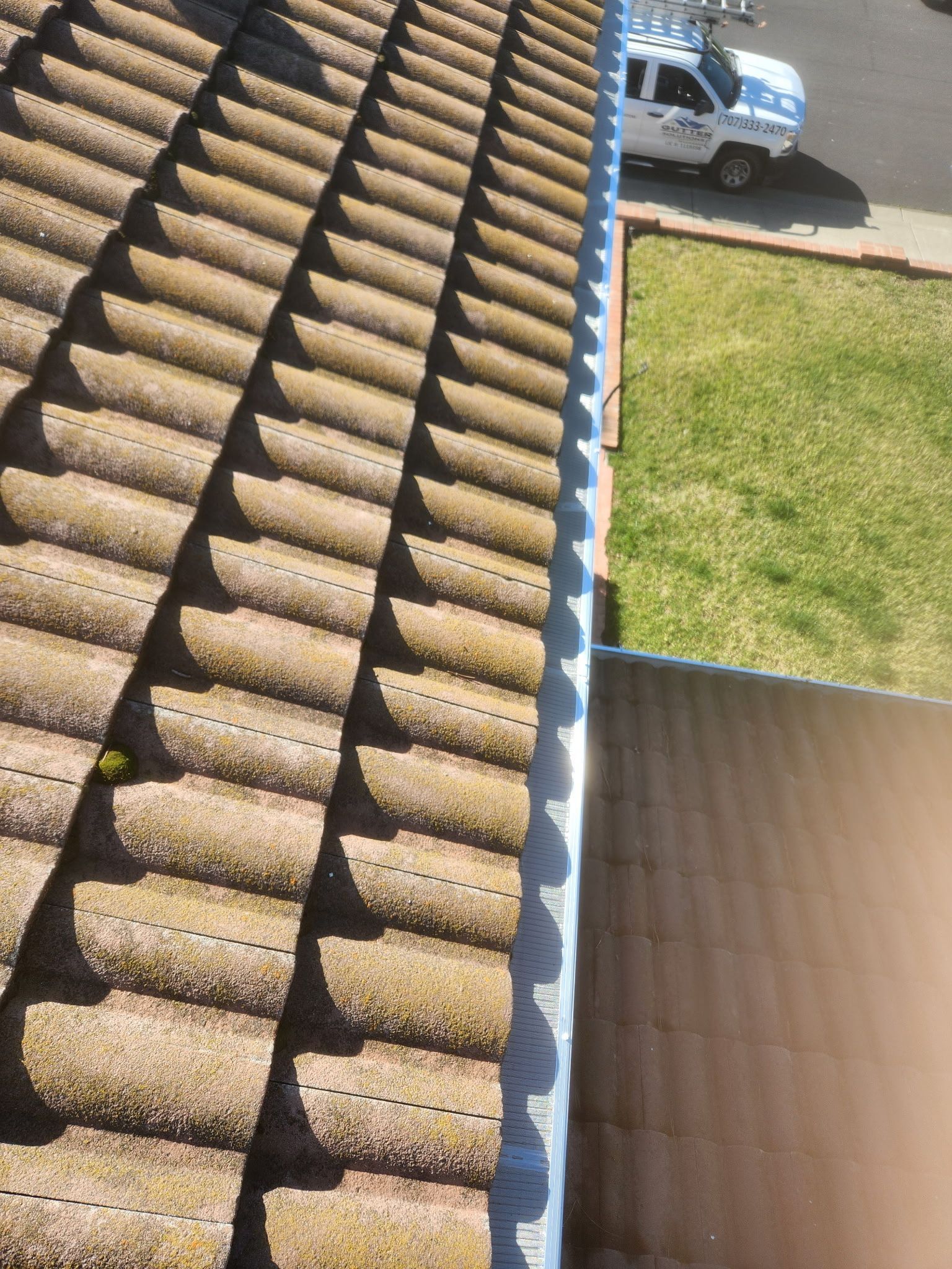Roof tiles with a damaged edge and a view of a driveway and lawn below