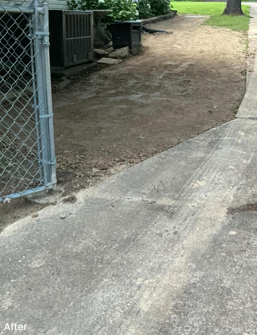 Concrete walkway beside a dirt patch leading to a fenced area with AC units.