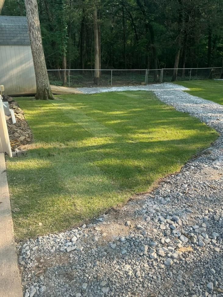 A green grassy area borders a gravel driveway, with trees in the background.