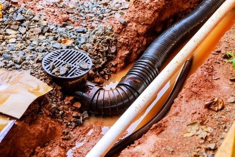 Drainage system installation with a grate, corrugated pipe, and PVC pipe in a trench.