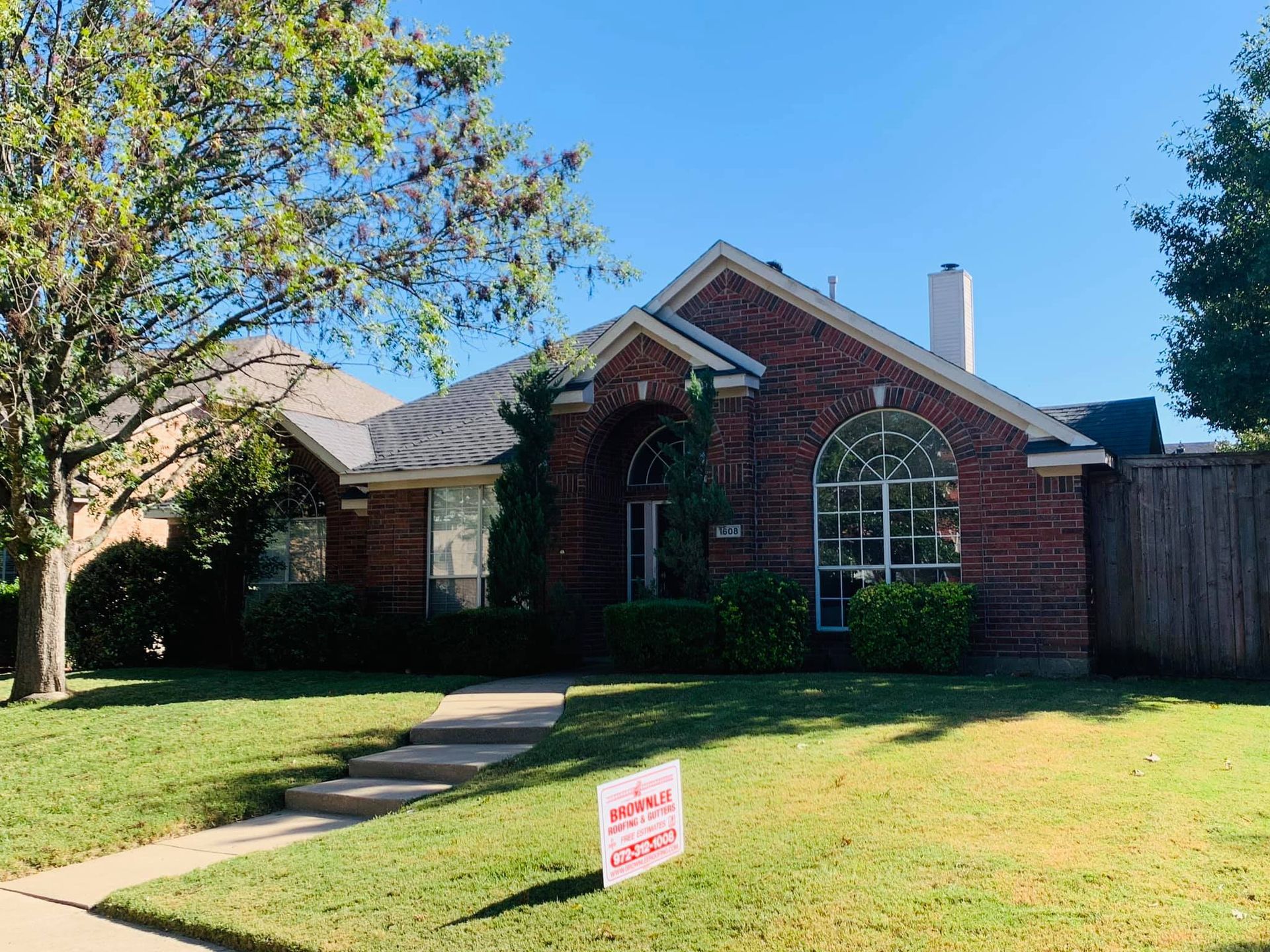 A brick house with a for sale sign in front of it.
