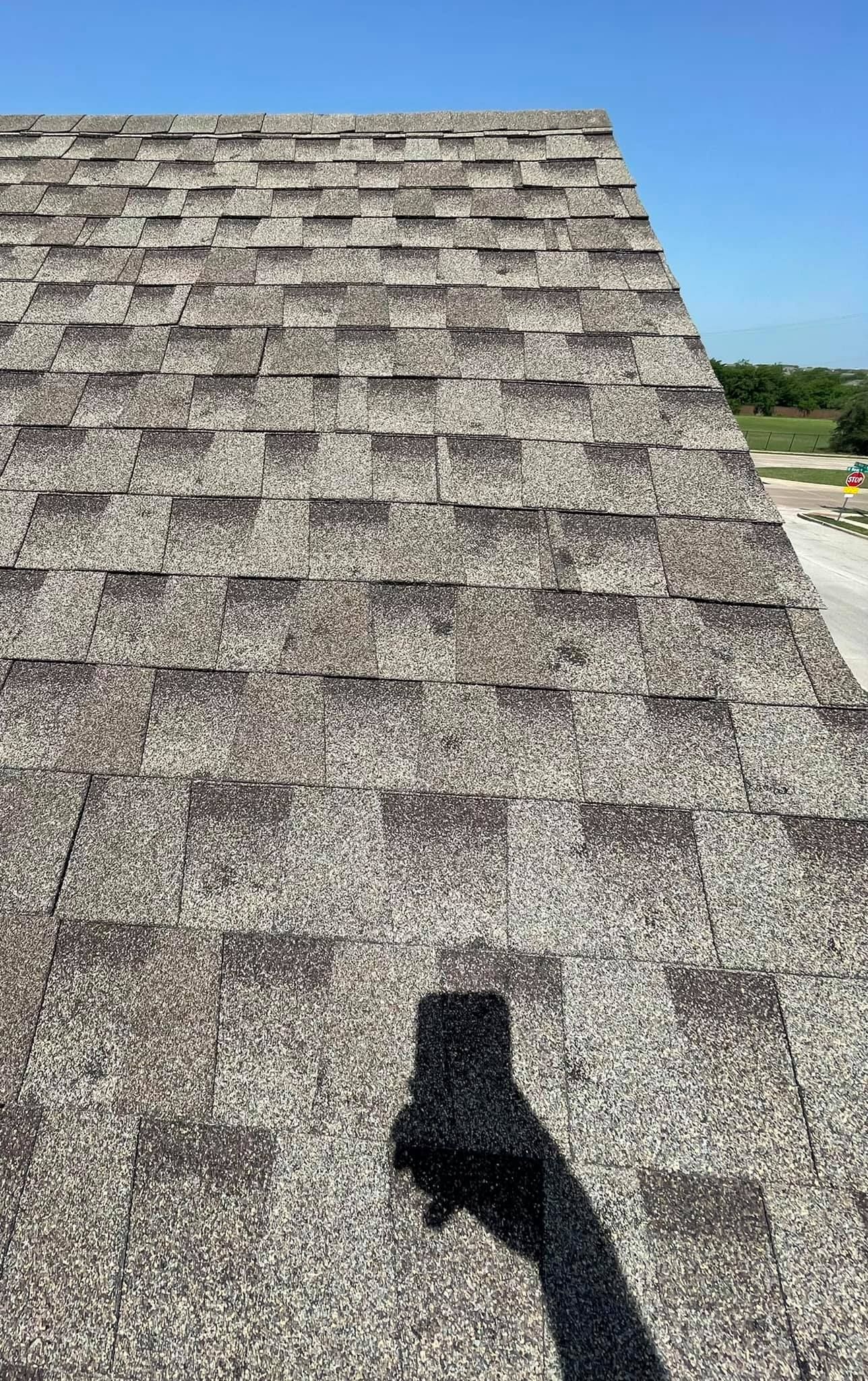 A roof with shingles and a shadow of a person on it.