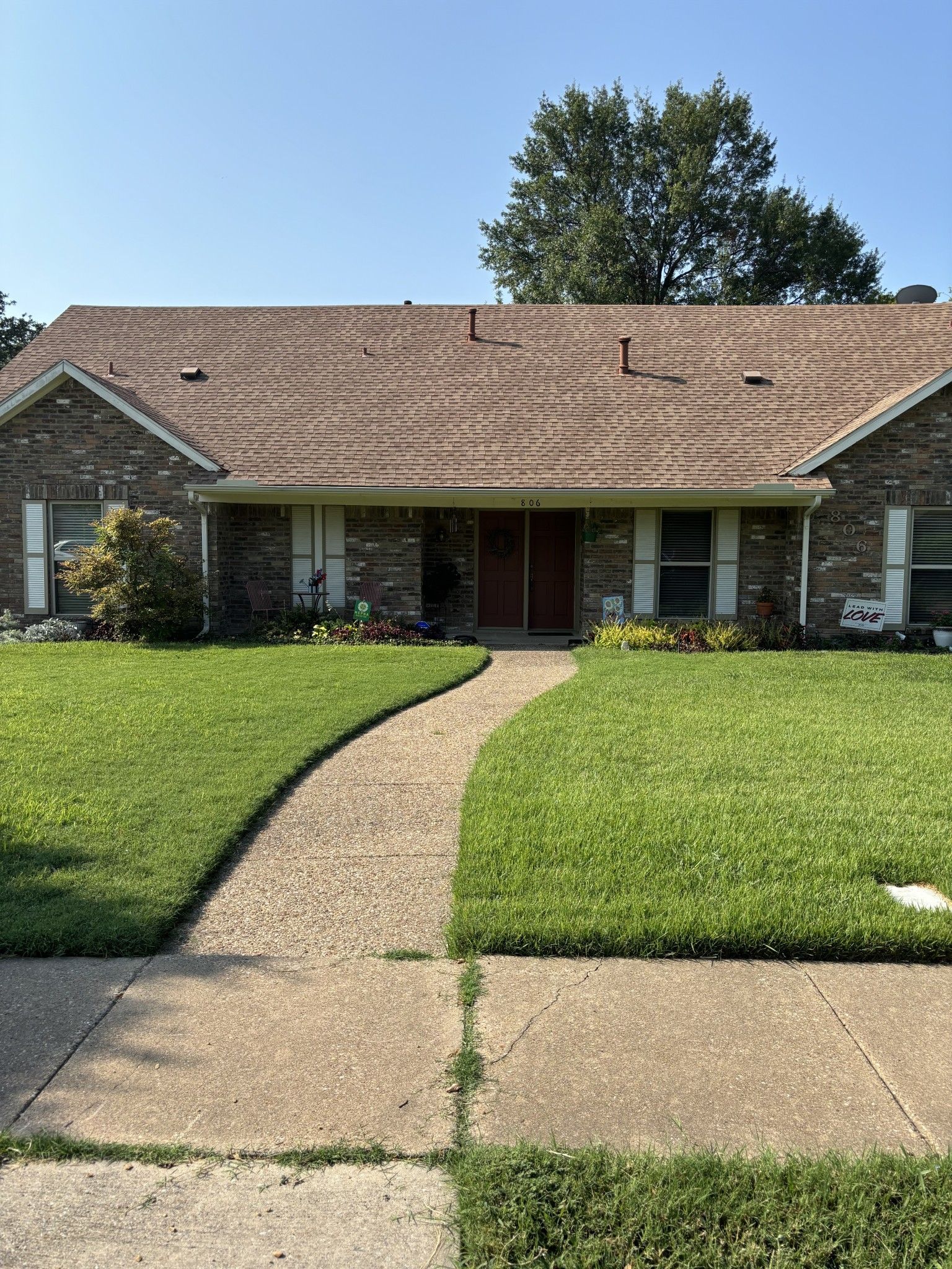 A brick house with a brown roof and a lush green lawn