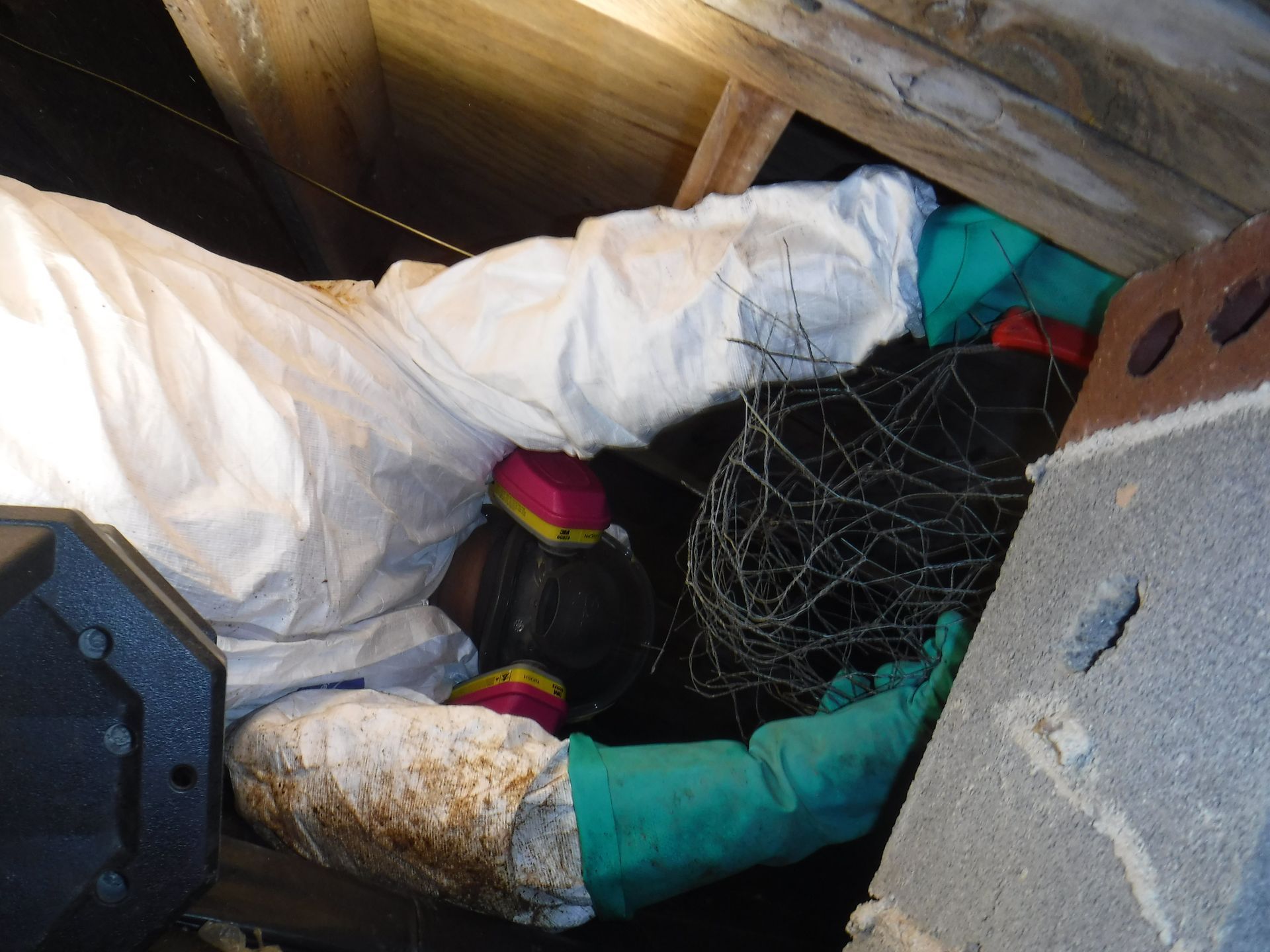 Person in protective suit, kneeling in crawlspace, working with wire.