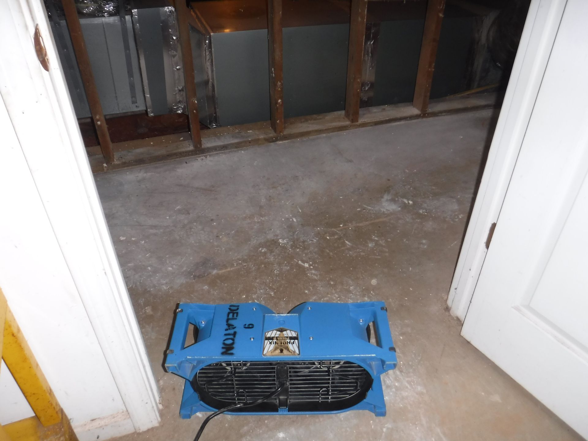 Blue air mover in a room with water damage on the concrete floor.