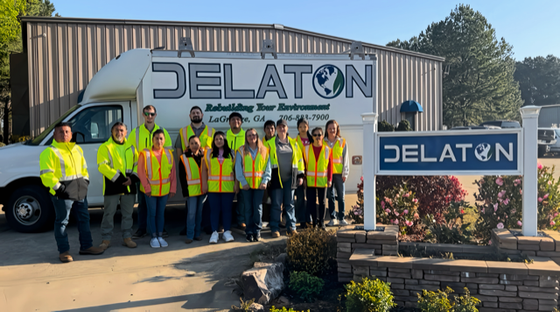 Group of people in safety vests in front of a white van with the Delaton logo and a Delaton sign.