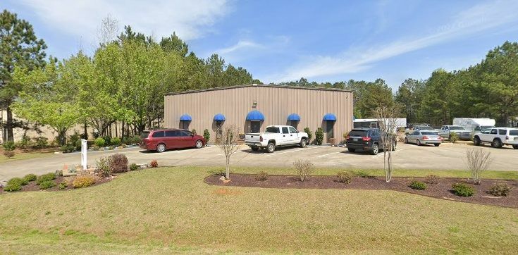 Building with blue awnings, cars parked in front, grass and trees surround it.