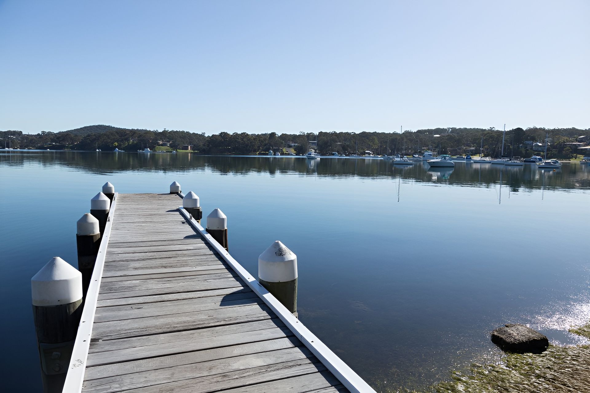 Wooden Pier Extending Into Calm Water, with Boats and Trees on The Distant Shore — M&J Marine Services in Lake Macquarie, NSW