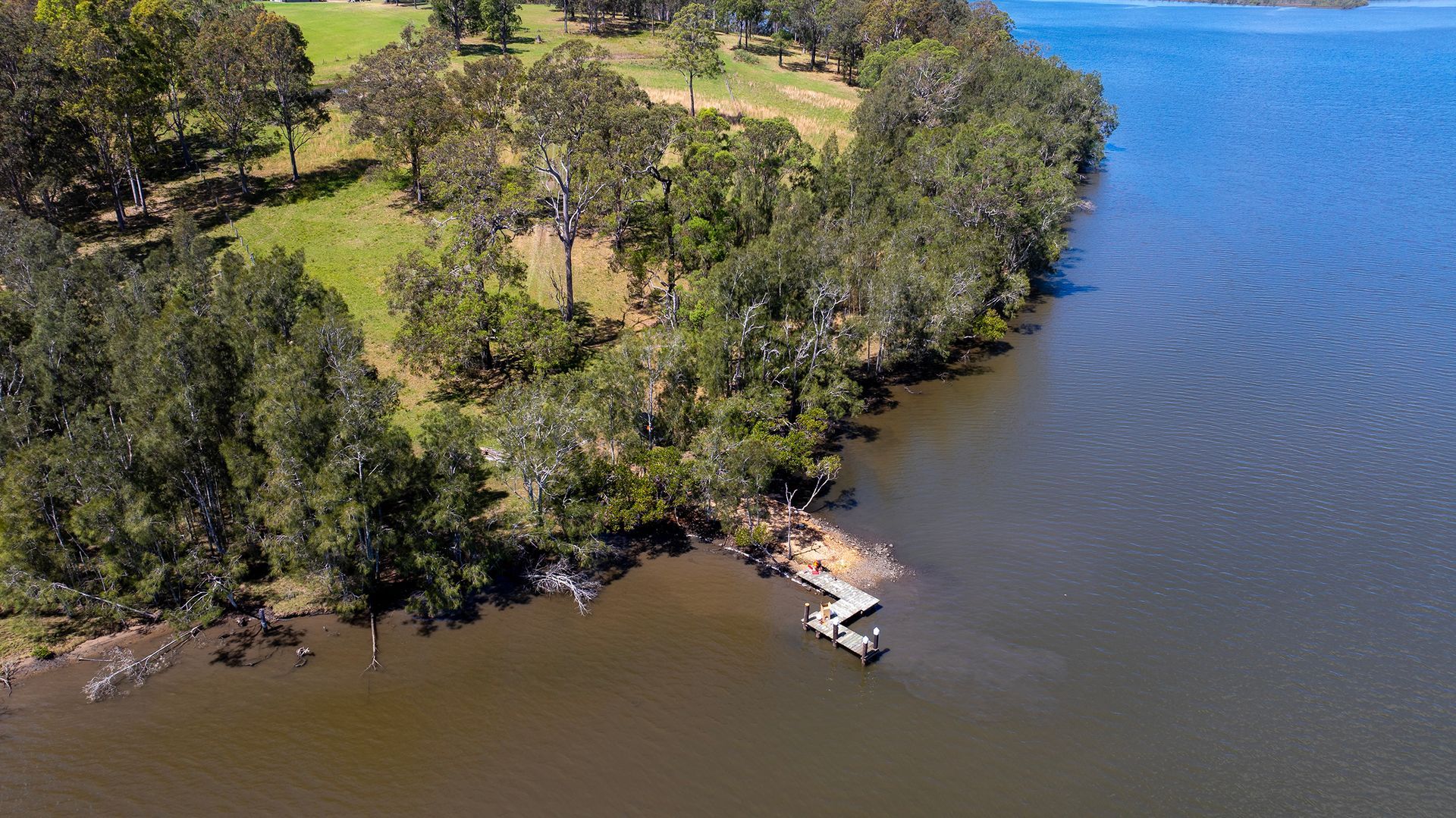 A Wooden Dock Extending from A Tree Lined Grassy Shoreline — M&J Marine Services in Lake Macquarie, NSW