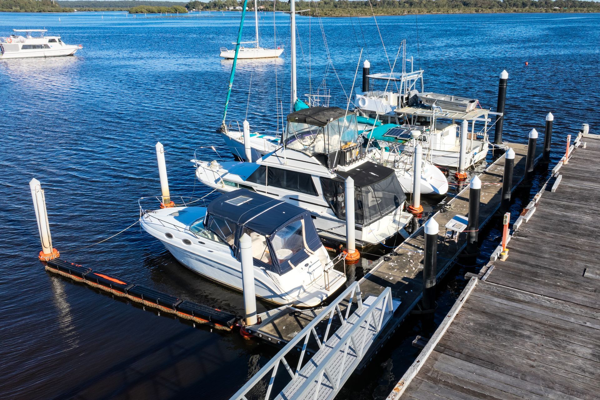 A Line of Powerboats and A Sailboat Docked at A Wooden Pier — M&J Marine Services in Medowie, NSW
