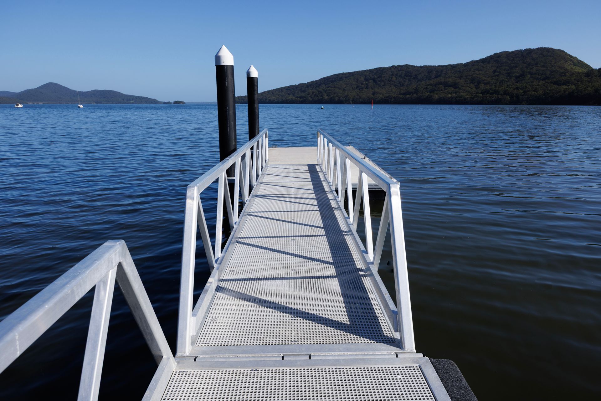 A White Metal Pier Stretches Into Calm Blue Water Toward a Distant — M&J Marine Services in Coffs Harbour, NSW