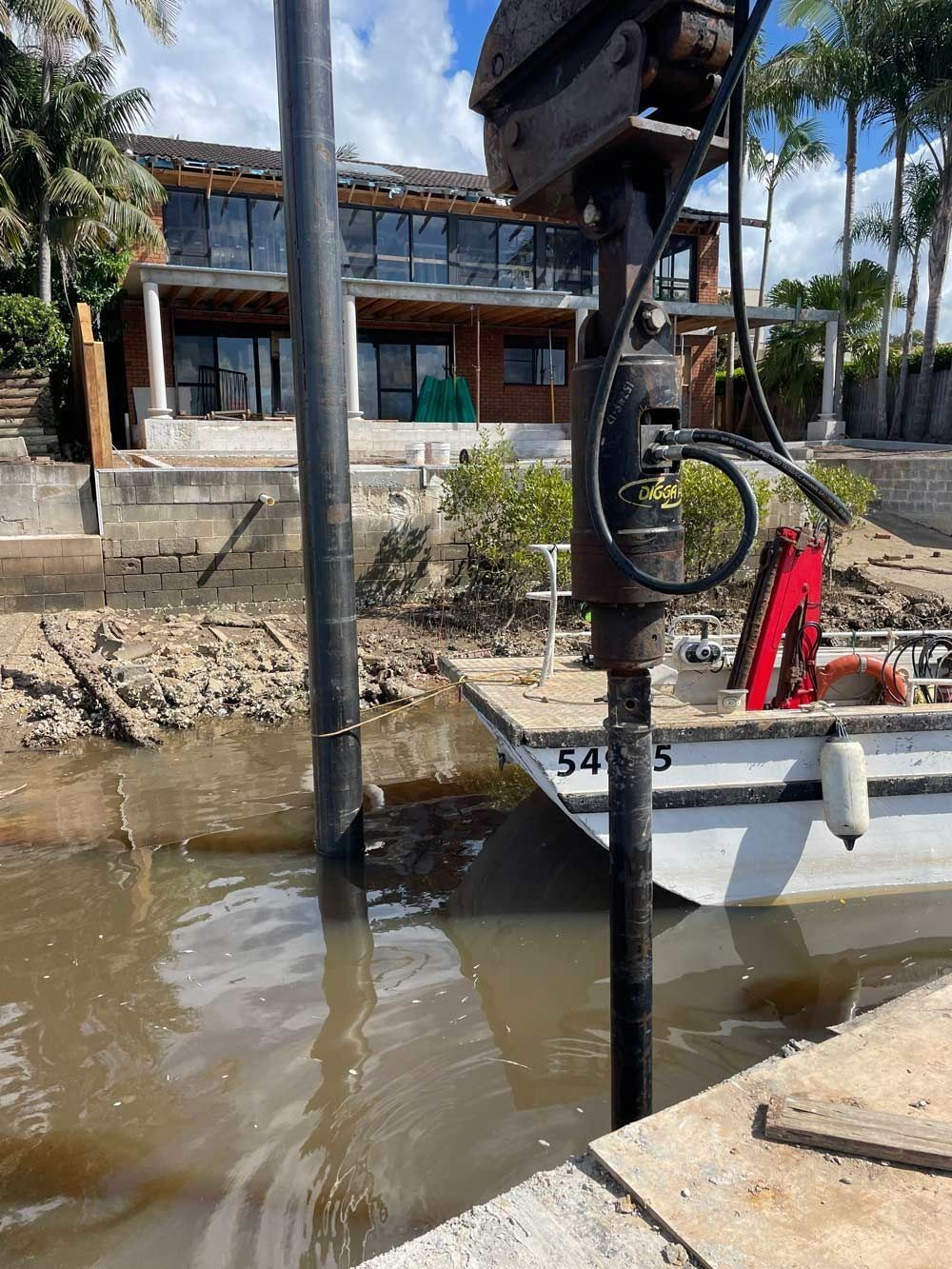 Construction Machinery Drilling Near Water with A House in The Background — M&J Marine Services in Newcastle, NSW