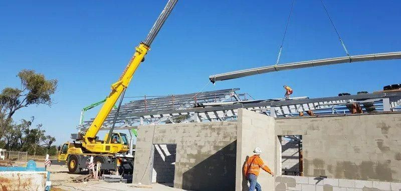A Crane Is Lifting A Beam On Top Of A Building Under Construction — Kosick Roofing NQ Pty Ltd In Mount Low, QLD