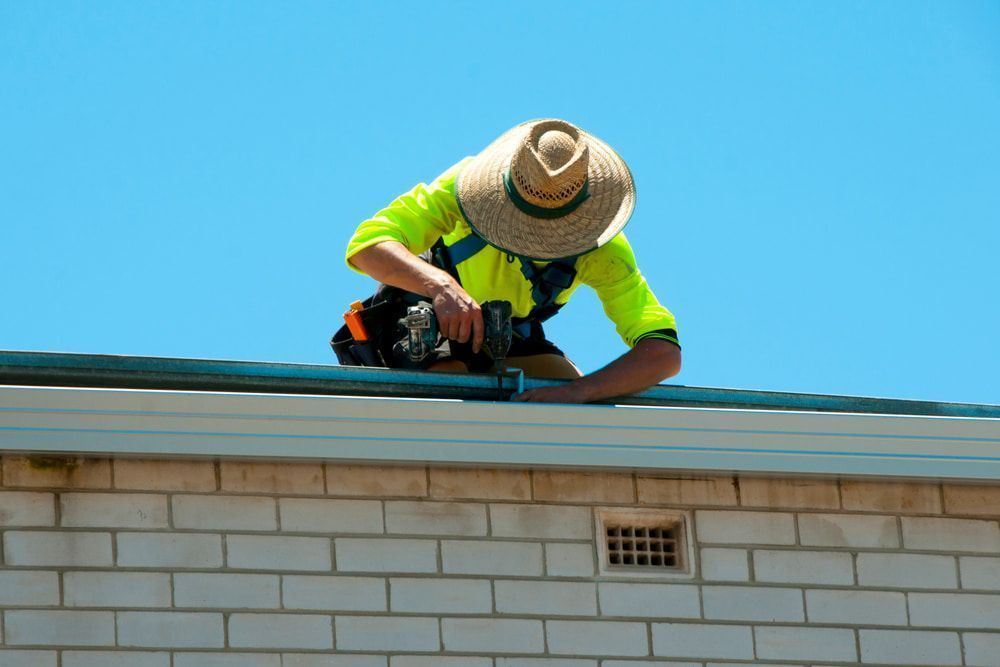 A Man Is Working On A Roof With A Drill — Kosick Roofing NQ Pty Ltd In Mount Low, QLD