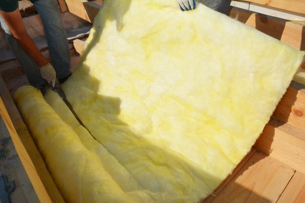 A Person Is Holding A Roll Of Yellow Insulation On A Wooden Floor — Kosick Roofing NQ Pty Ltd In Mount Low, QLD