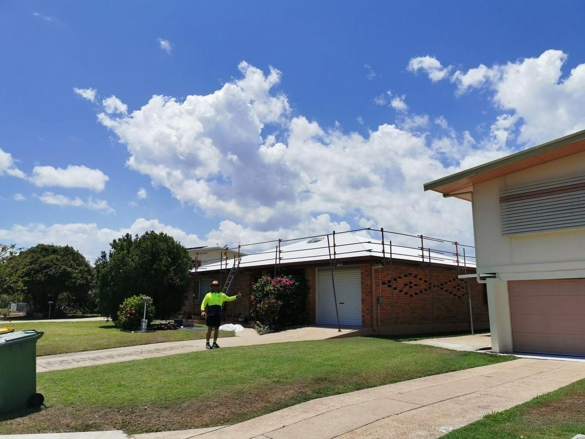 A Man In A Yellow Vest Is Standing In Front Of A House — Kosick Roofing NQ Pty Ltd In Mount Low, QLD