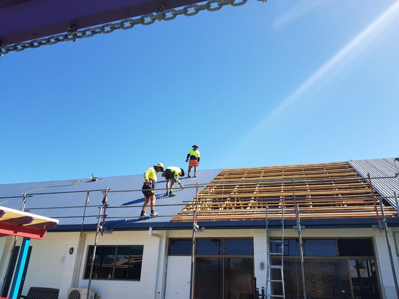 A Group Of Men Are Working On The Roof Of A Building — Kosick Roofing NQ Pty Ltd In Mount Low, QLD
