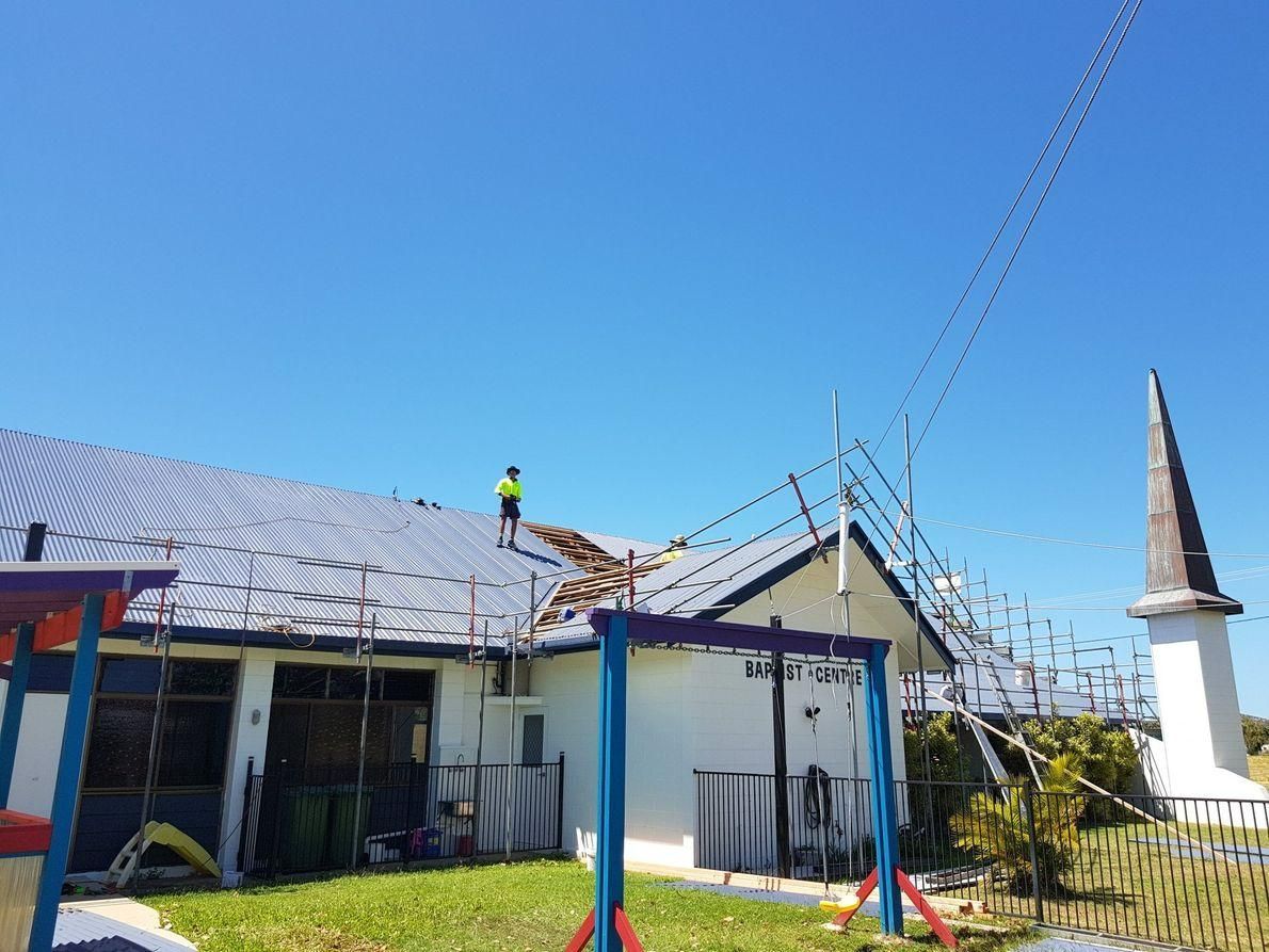 A Man Is Standing On The Roof Of A House — Kosick Roofing NQ Pty Ltd In Mount Low, QLD