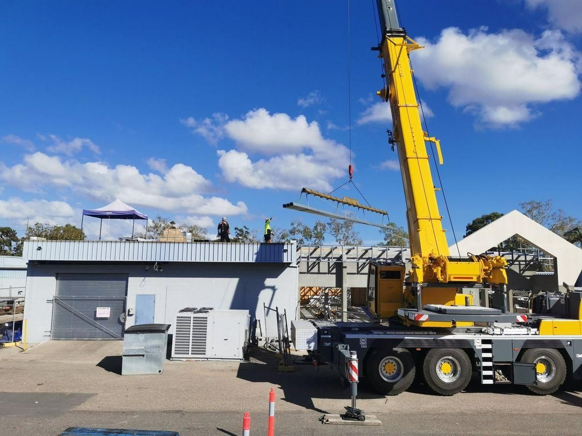 A Large Yellow Crane Is Sitting In Front Of A Building — Kosick Roofing NQ Pty Ltd In Mount Low, QLD