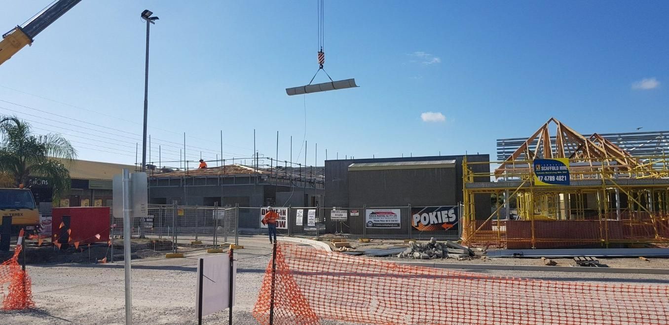 A Crane Is Lifting A Piece Of Metal In The Air At A Construction Site — Kosick Roofing NQ Pty Ltd In Mount Low, QLD
