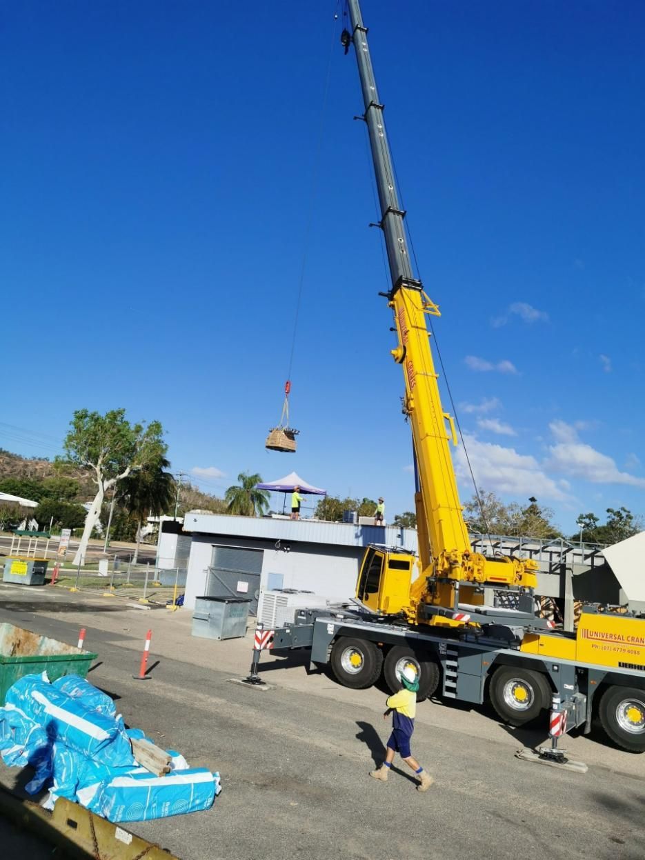 A Large Yellow Crane Is Lifting A Large Object On Top Of A Building — Kosick Roofing NQ Pty Ltd In Mount Low, QLD