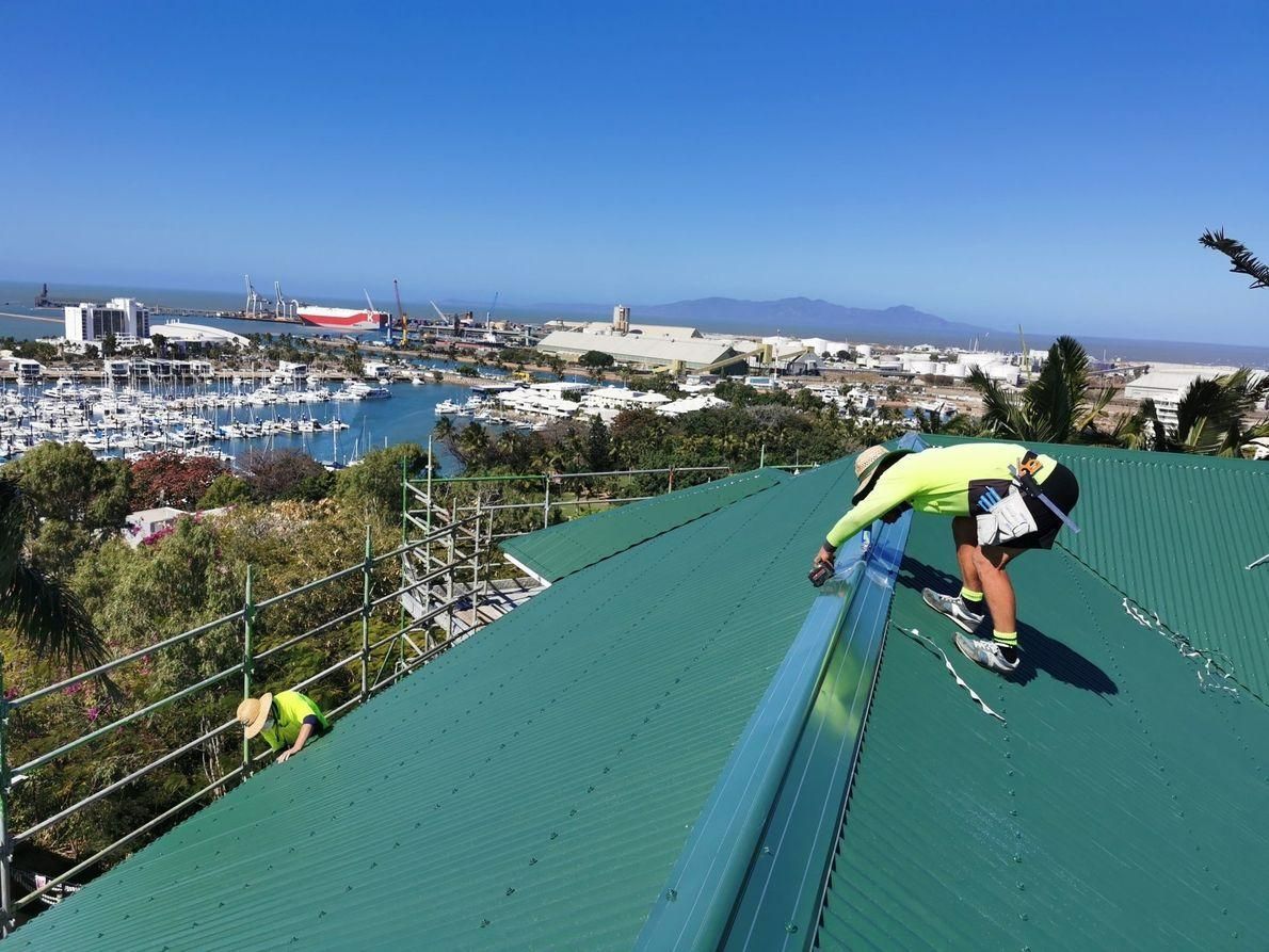 A Man Is Working On The Roof Of A Building — Kosick Roofing NQ Pty Ltd In Mount Low, QLD