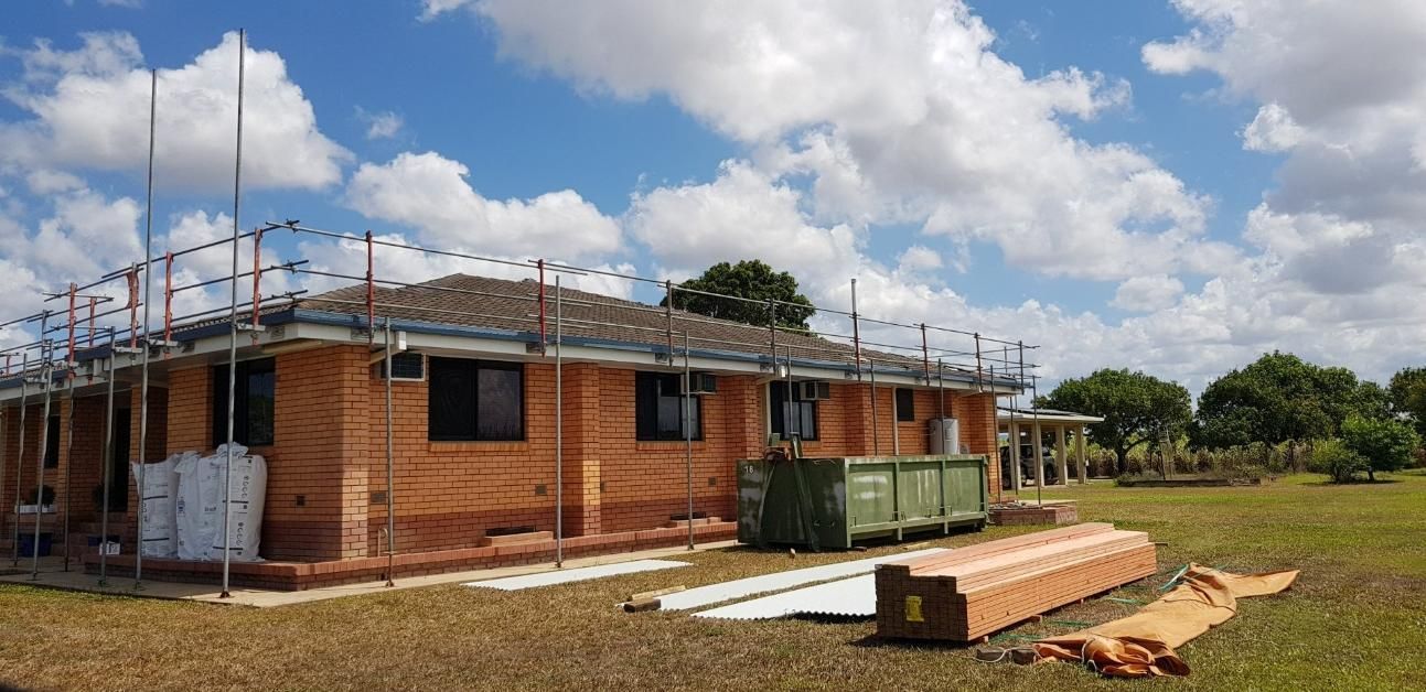 A Brick House Is Being Built In A Field With Scaffolding — Kosick Roofing NQ Pty Ltd In Mount Low, QLD