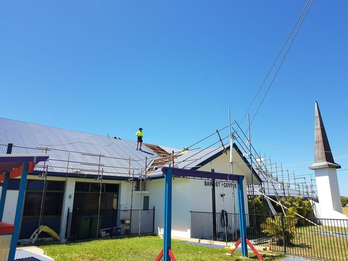 A Man Is Standing On The Roof Of A House — Kosick Roofing NQ Pty Ltd In Mount Low, QLD