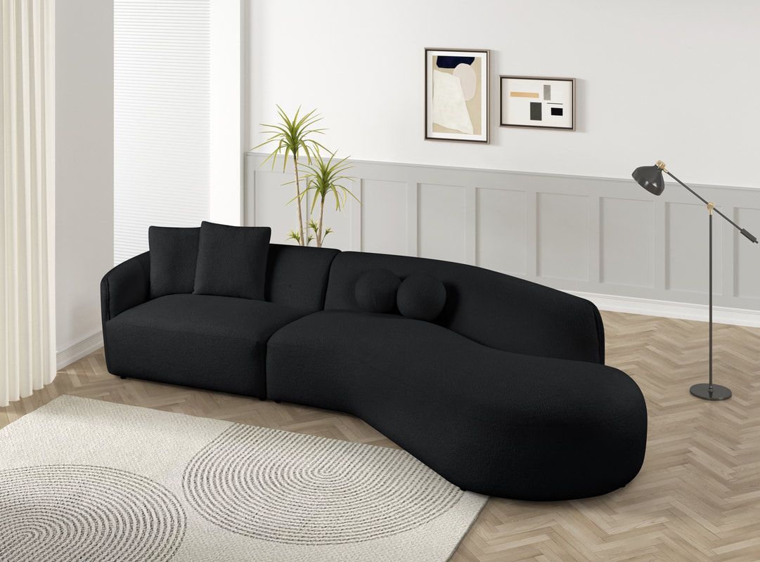 A black couch is sitting in a living room next to a lamp.