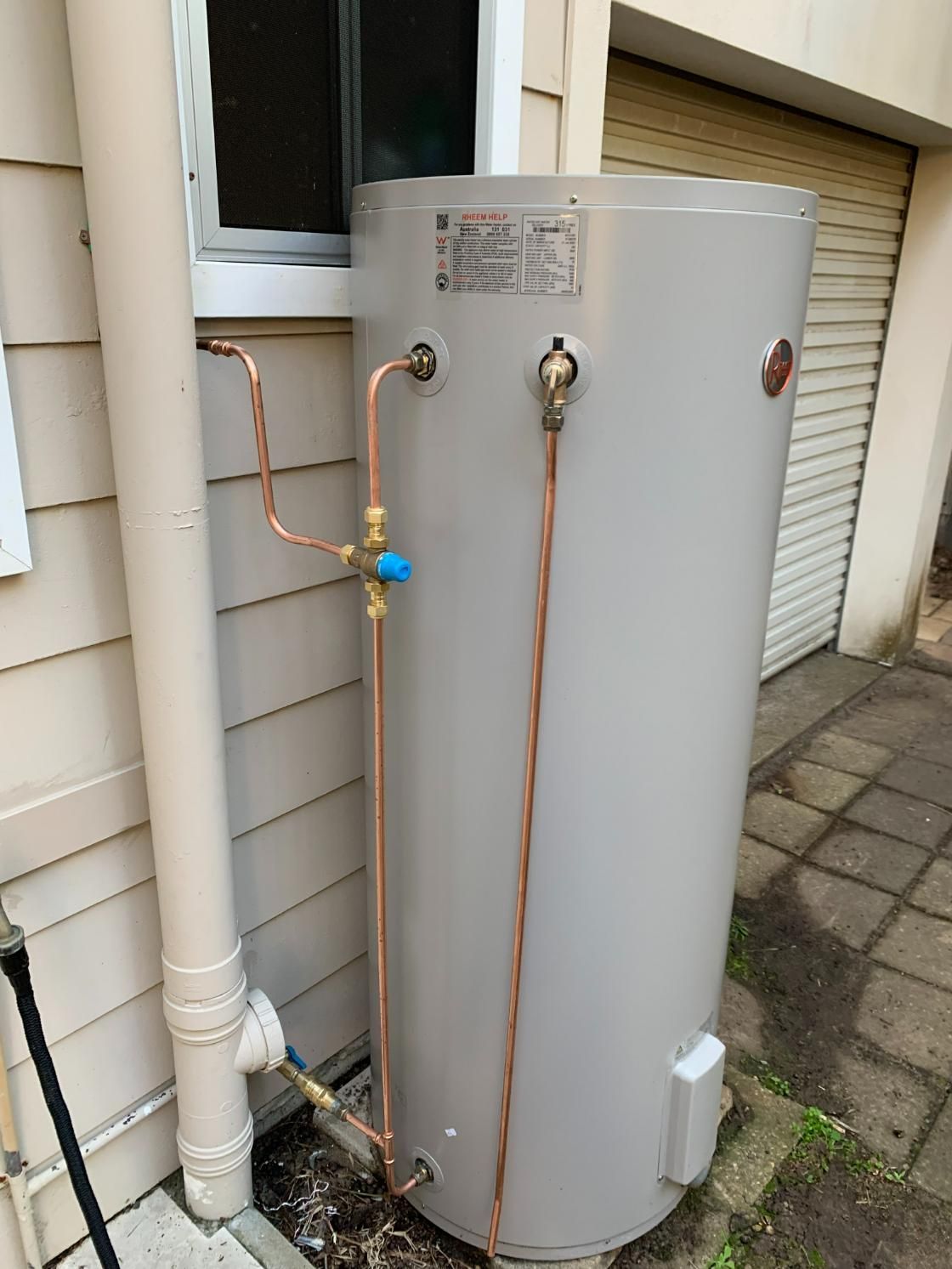A Water Heater Is Sitting On The Side Of A House Next To A Window — Oceanforce Plumbing In Blacksmiths, NSW