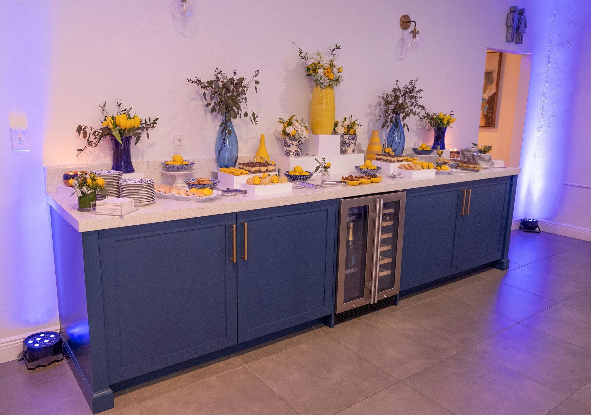 A long buffet table with blue cabinets and a stainless steel refrigerator.