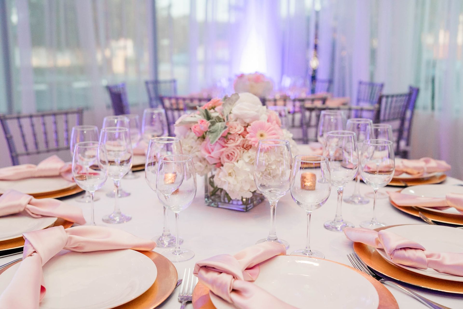 A table set for a wedding reception with plates , glasses , napkins and a vase of flowers.