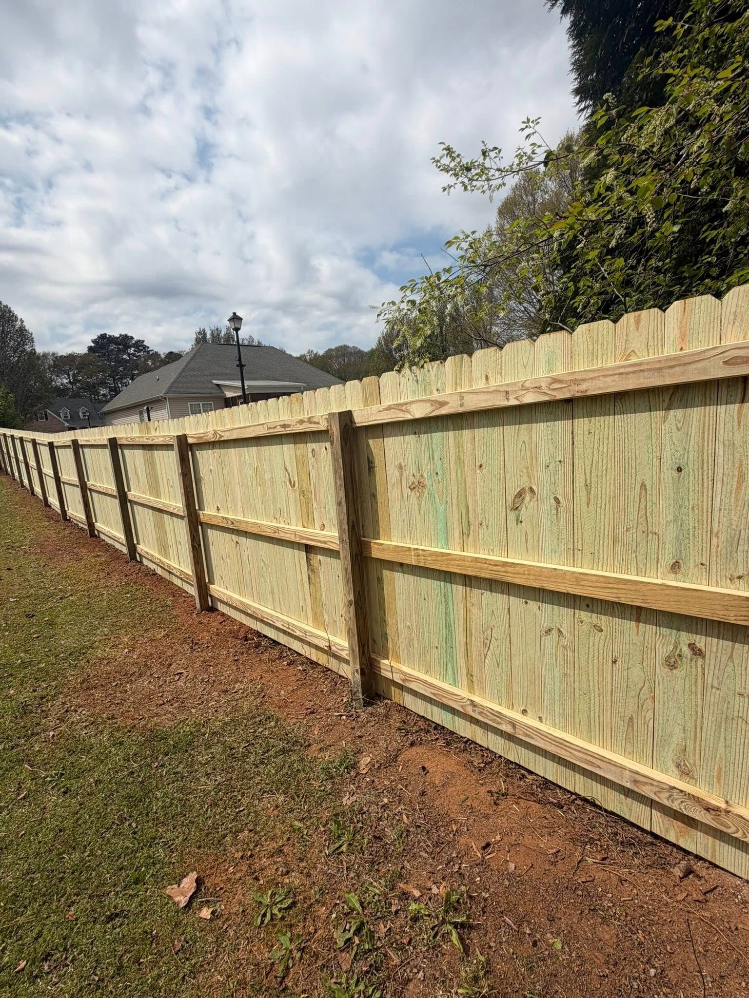 A new, light-colored wooden fence runs along the edge of a grassy lawn under a partly cloudy sky.