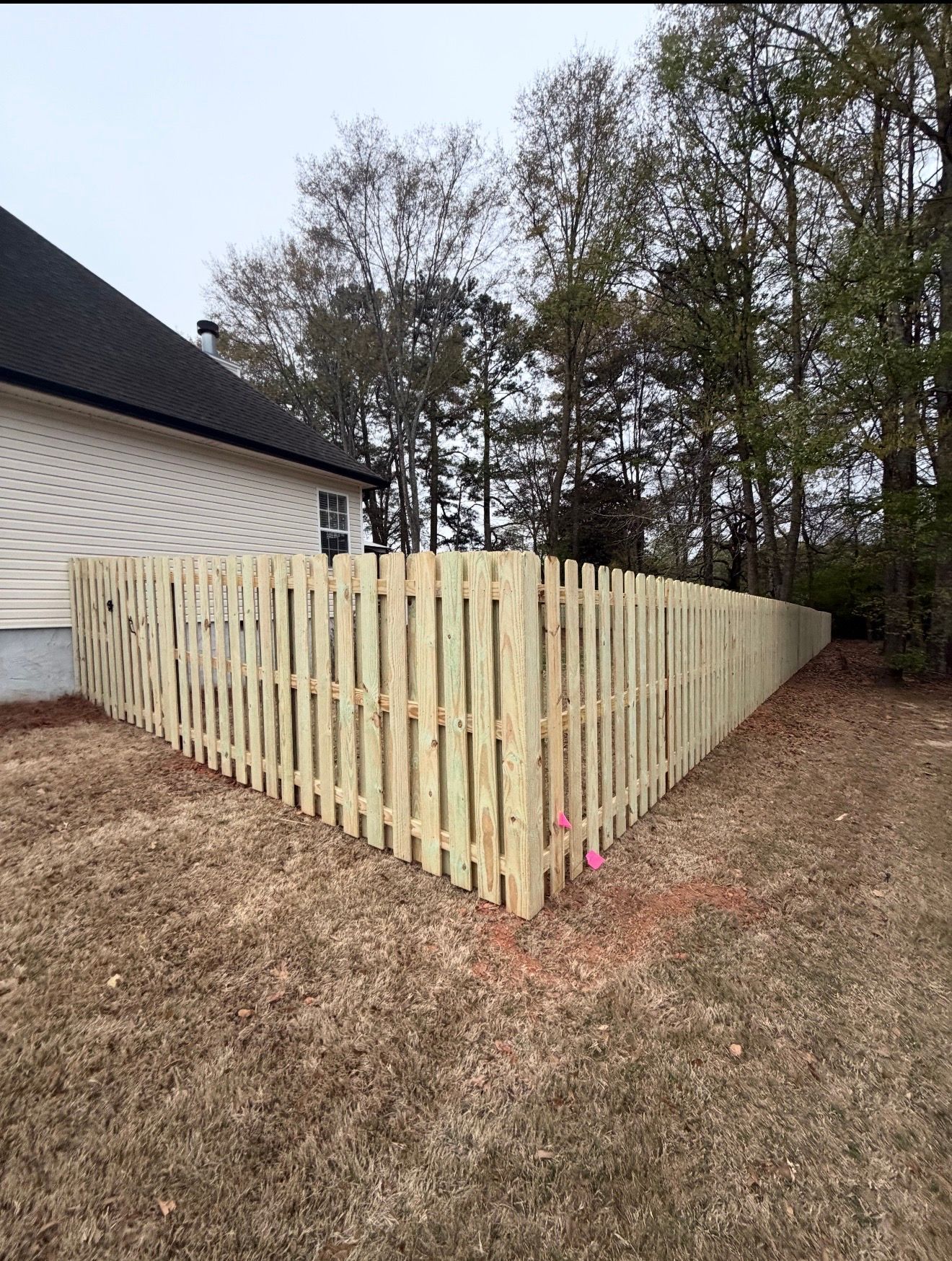 Newly built wooden privacy fence around a backyard beside a house and trees