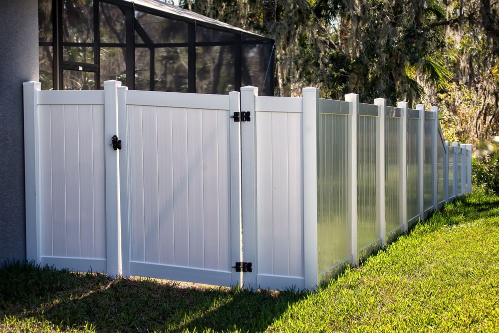 A white vinyl privacy fence with a matching gate, installed in a grassy backyard next to a screened-in enclosure.