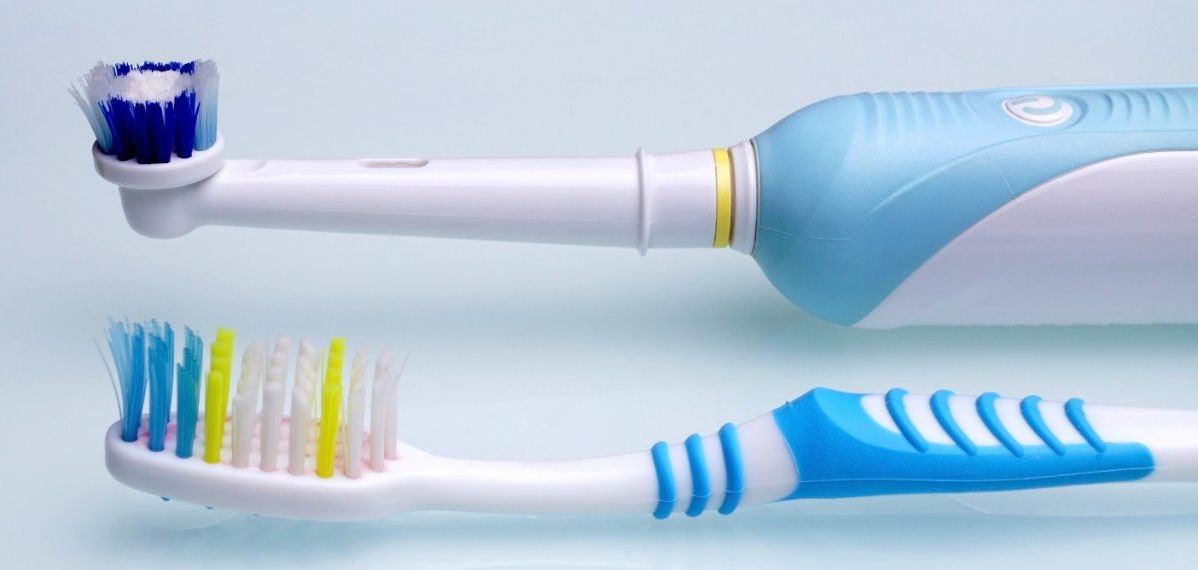 A toothbrush and an electric toothbrush are next to each other on a blue surface.