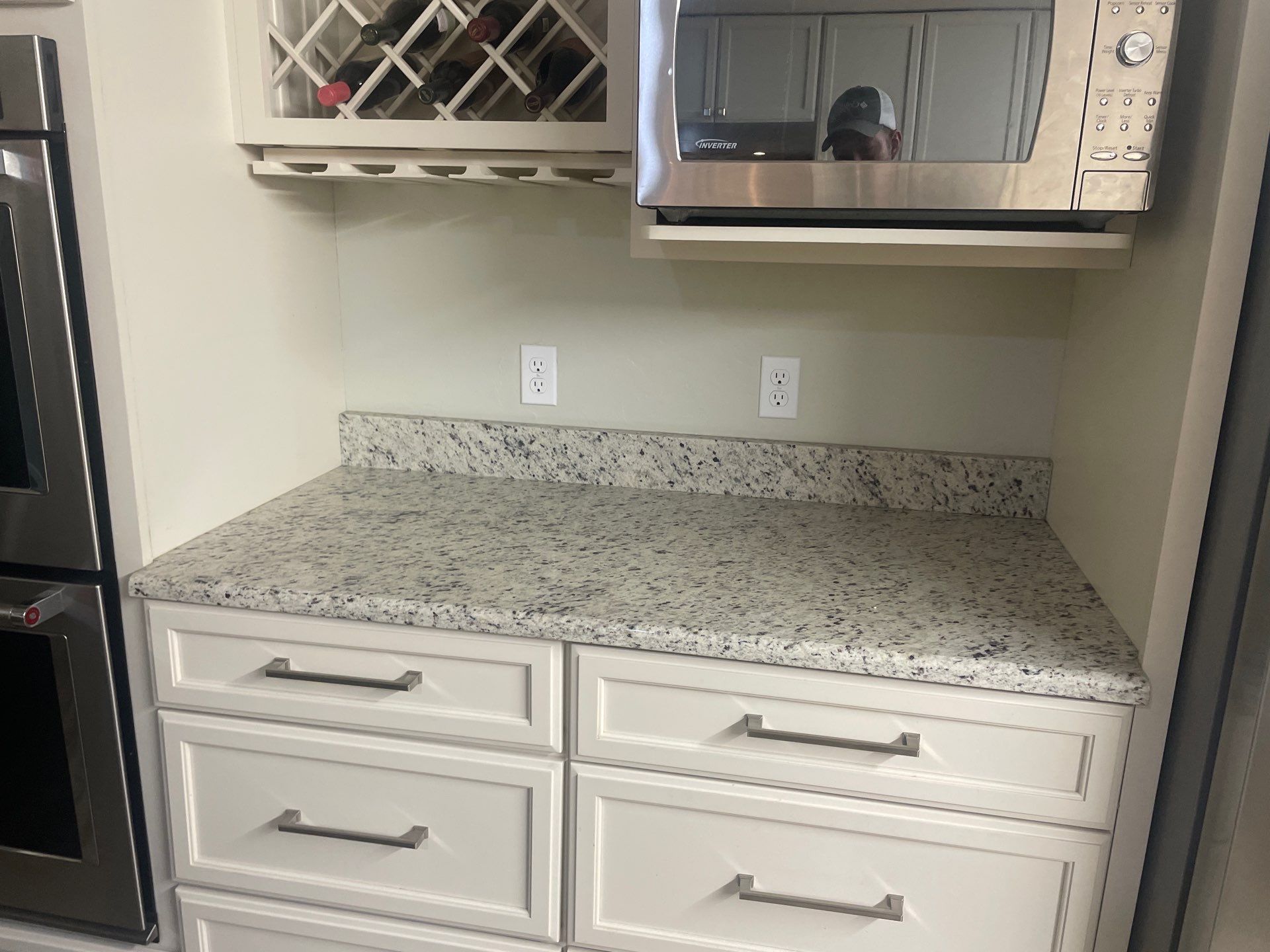 A kitchen with white cabinets , granite counter tops , stainless steel appliances and a wine rack.
