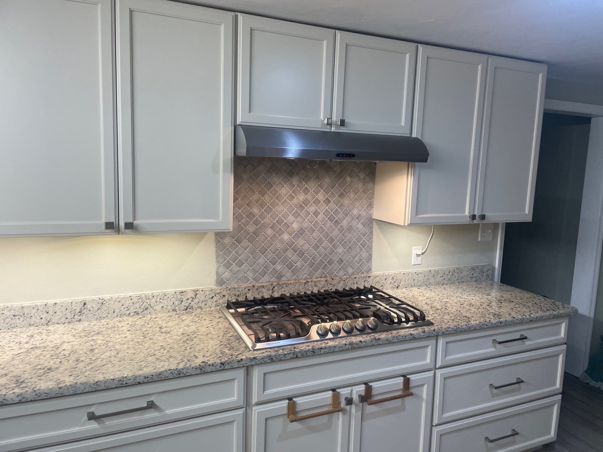 A kitchen with white cabinets , granite counter tops , and a stove top oven.