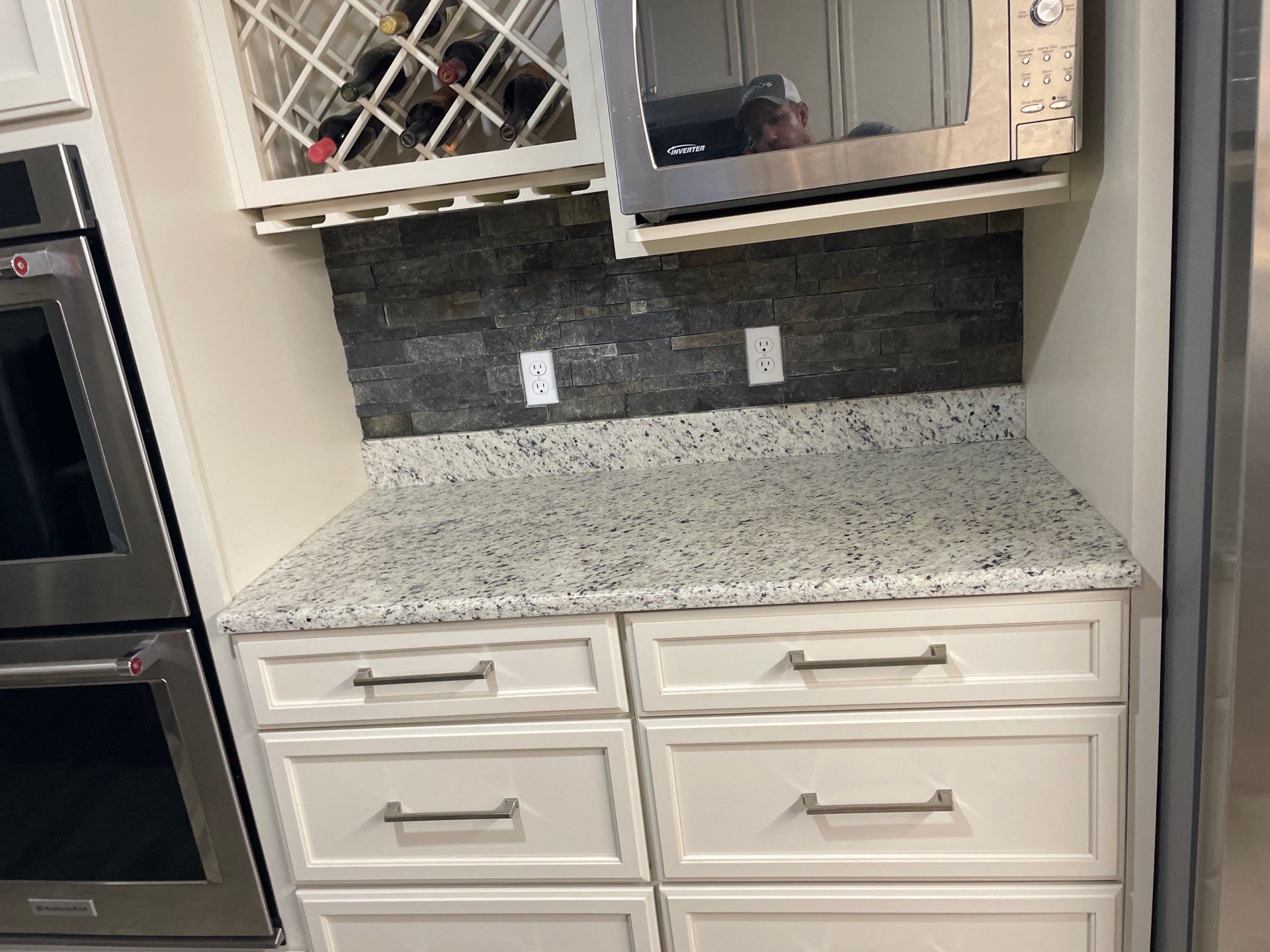 A kitchen with white cabinets , granite counter tops , stainless steel appliances and a wine rack.